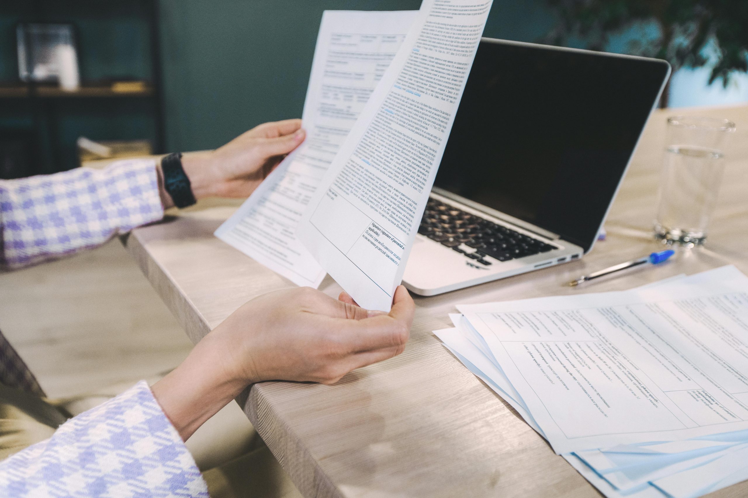 Close-up of hands examining printed documents next to laptop on office desk.